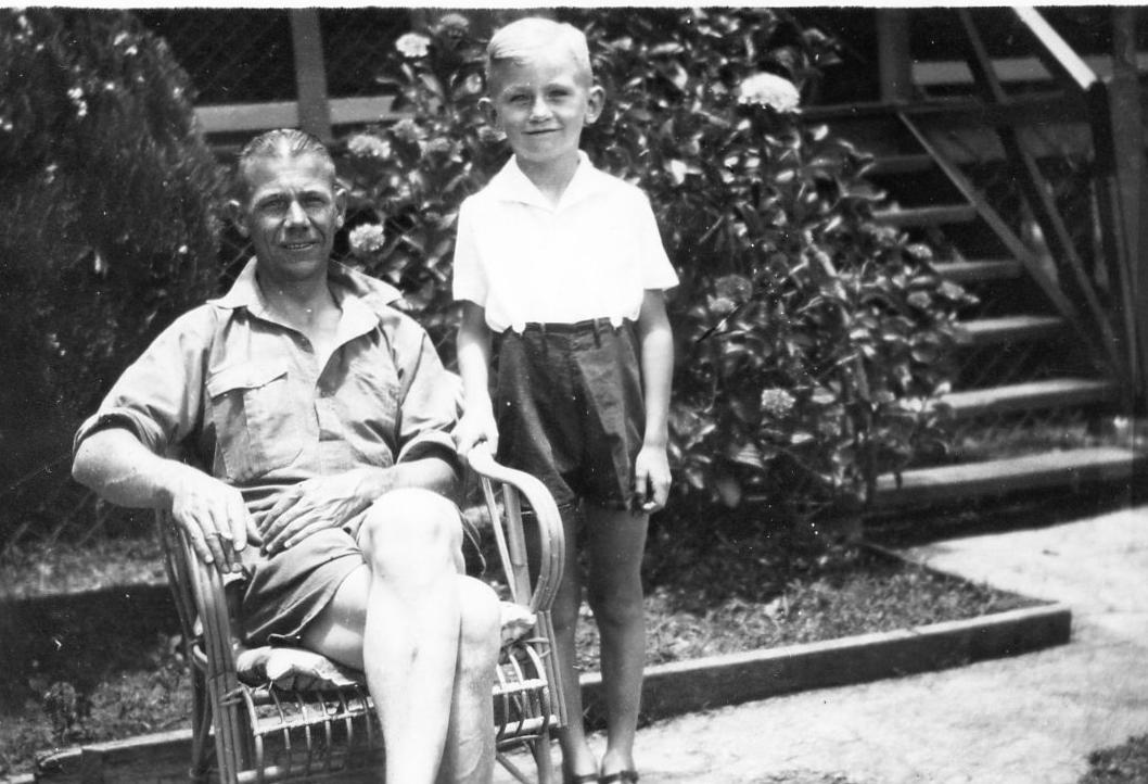 Junior in the front yard with Dad; hydrangea bush and front veranda with steps behind.
